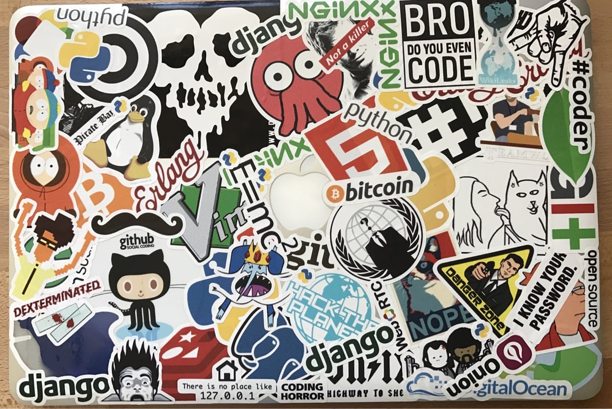 Laptop sticker collage featuring tech and programming references including GitHub, Python, Bitcoin, Django, and Linux logos mixed with internet culture imagery.
