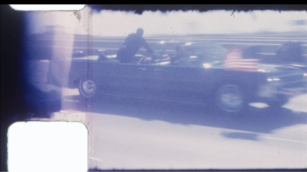 a blurry film still showing a large black convertible speeding by on a freeway