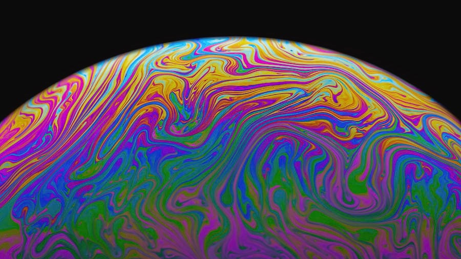 the swirling rainbow surface of a soap bubble from close-up looks like a small planet