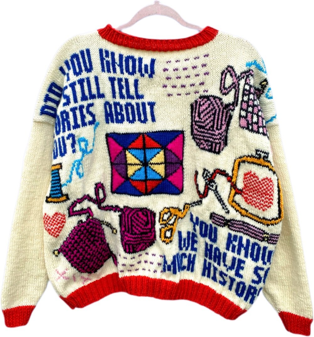 a cream-colored sweater with lots of words and objects knitted into it
