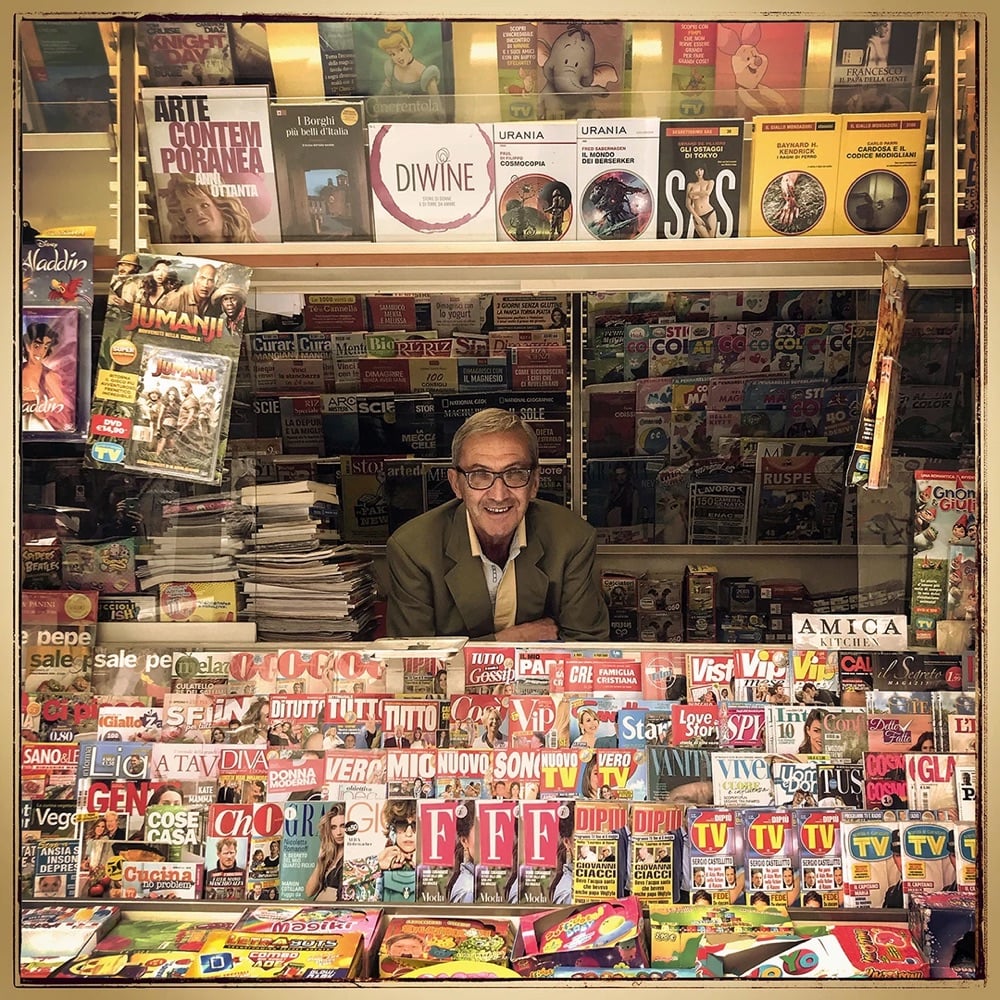 a smiling newsseller looks out of his newsstand
