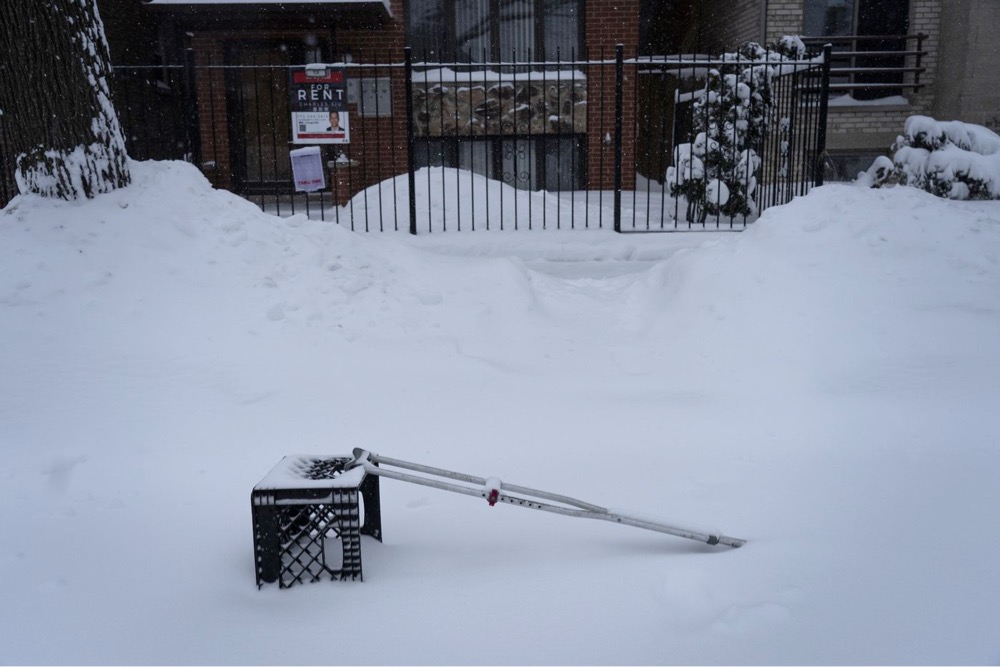 a crutch and a milkcrate placed in a shoveled-out parking spot
