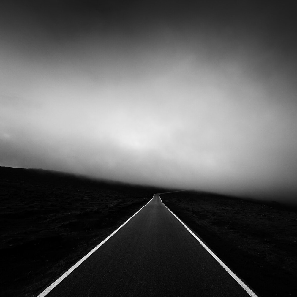 a dark road disappears into a cloud in the distance